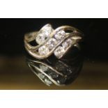 A WHITE METAL AND DIAMOND SEVEN STONE RING With an arrangement of round cut diamonds set on a curved