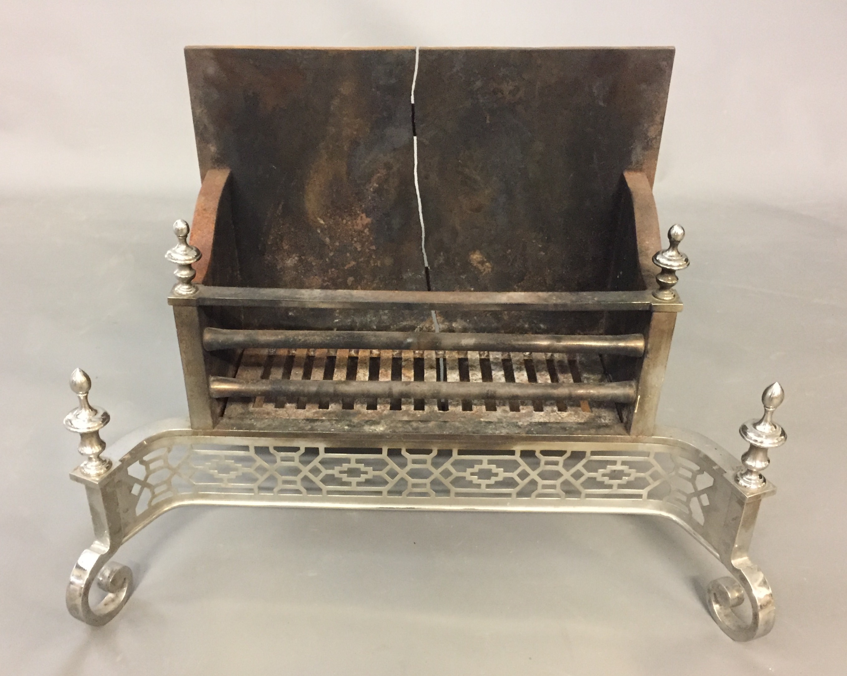 A REGENCY DESIGN POLISHED STEEL FIRE GRATE With turned finials and pierced fretwork apron, raised on