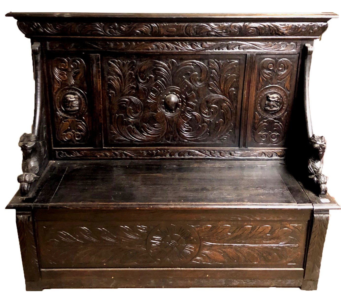 A VICTORIAN CARVED OAK SETTLE Heavily carved with Medieval style scrolls and masks, on recumbent