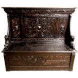 A VICTORIAN CARVED OAK SETTLE Heavily carved with Medieval style scrolls and masks, on recumbent