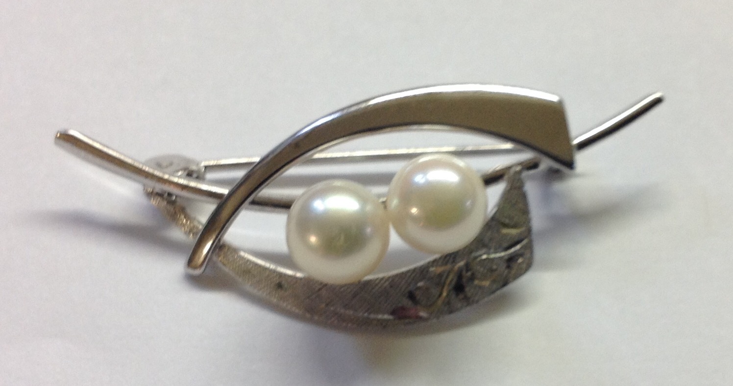 A VINTAGE SILVER AND CULTURED PEARL BROOCH The two white pearls prong set to a curved bar, decorated