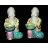 A PAIR OF FAMILLE ROSE KNEELING SAGES Each bearded figure holding a peach form cup and wearing