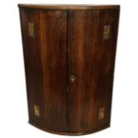 A GEORGIAN OAK HANGING CORNER CABINET With brass fittings and shelved interior. (h 84.5 x d 60cm)
