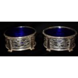 OMAR RAMSDEN, 1873 - 1939, A PAIR OF ARTS & CRAFTS STYLE SILVER AND BLUE GLASS SALTS With Celtic