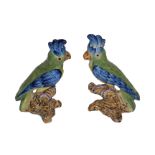 A PAIR OF 20TH CENTURY FAIENCE POTTERY PARROTS Painted with blue green feathers and perched on a