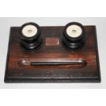 AN EDWARDIAN OAK COMMEMORATIVE DESK STAND INKWELL Set with two ceramic inkwells and bearing a