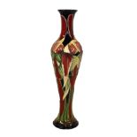 MOORCROFT, A SLENDER TUBELINED POTTERY VASE Decorated with stylized blue and red flowers, signed