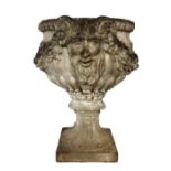 A GRECIAN DESIGN FAUX STONE URN Cast with horned masked and foliage. (59cm x 38cm x 52cm)