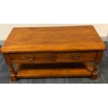AN OAK COFFEE TABLE With double sided drawers and an open shelf, raised on turned legs. (w 110cm x d