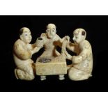 A 19TH CENTURY IVORY NETSUKE Carved as three performing a tea ceremony. (h 2.8cm)