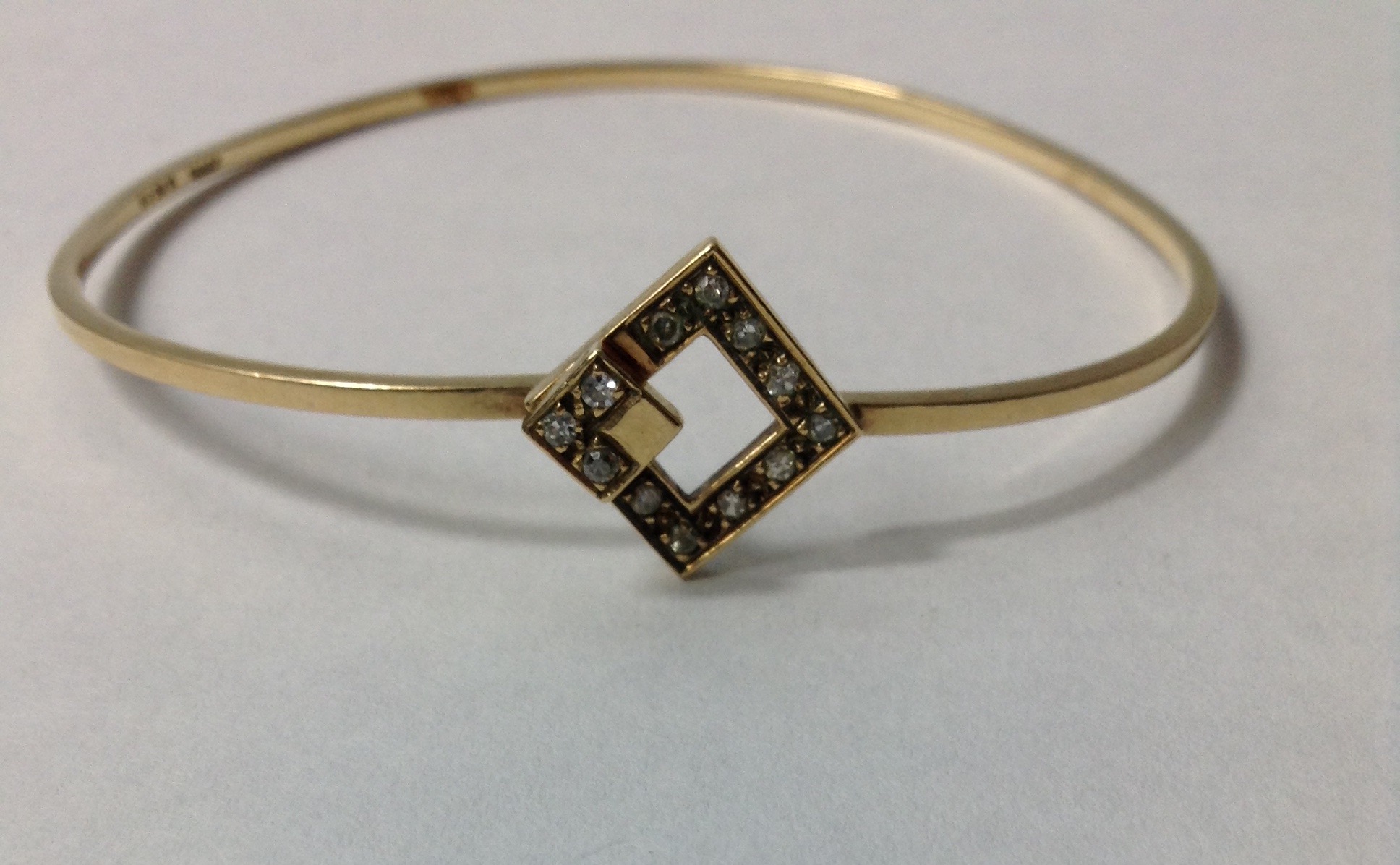 A VINTAGE 9CT GOLD AND DIAMOND BANGLE The single row of diamonds in a geometric design. (approx