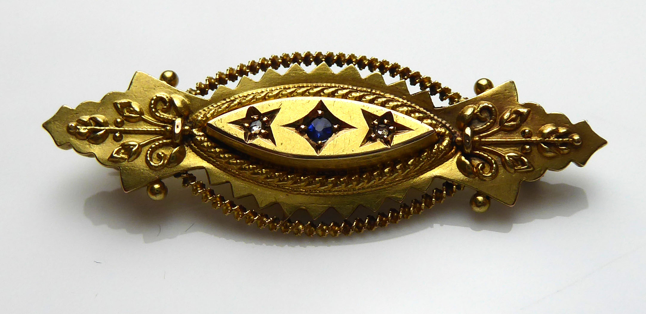 A VICTORIAN 15CT GOLD, SAPPHIRE AND DIAMOND BROOCH The single sapphire flanked by diamonds in a