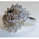 A WHITE METAL AND DIAMOND CLUSTER RING Having a single round cut diamond, flanked by a row of