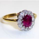 A VINTAGE YELLOW METAL, NATURAL RUBY AND DIAMOND CLUSTER RING Having an oval cut ruby, surrounded by