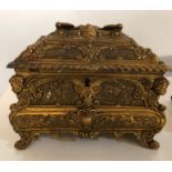 TWO EARLY 20TH CENTURY GILT METAL TABLE CASKETS With relief scenes and cherub masks (17cm x 14cm x