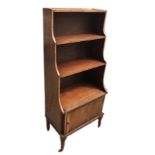 AN EARLY 20TH CENTURY REGENCY DESIGN MAHOGANY WATERFALL BOOKCASE The open shelves above cupboard,