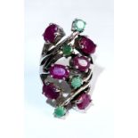 AN UNUSUAL WHITE METAL, EMERALD AND RUBY RING The arrangement of stones held in a pierced design (