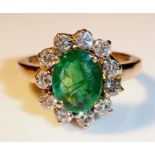 AN 18CT GOLD, EMERALD AND DIAMOND CLUSTER RING Having a faceted oval cut emerald flanked by eleven