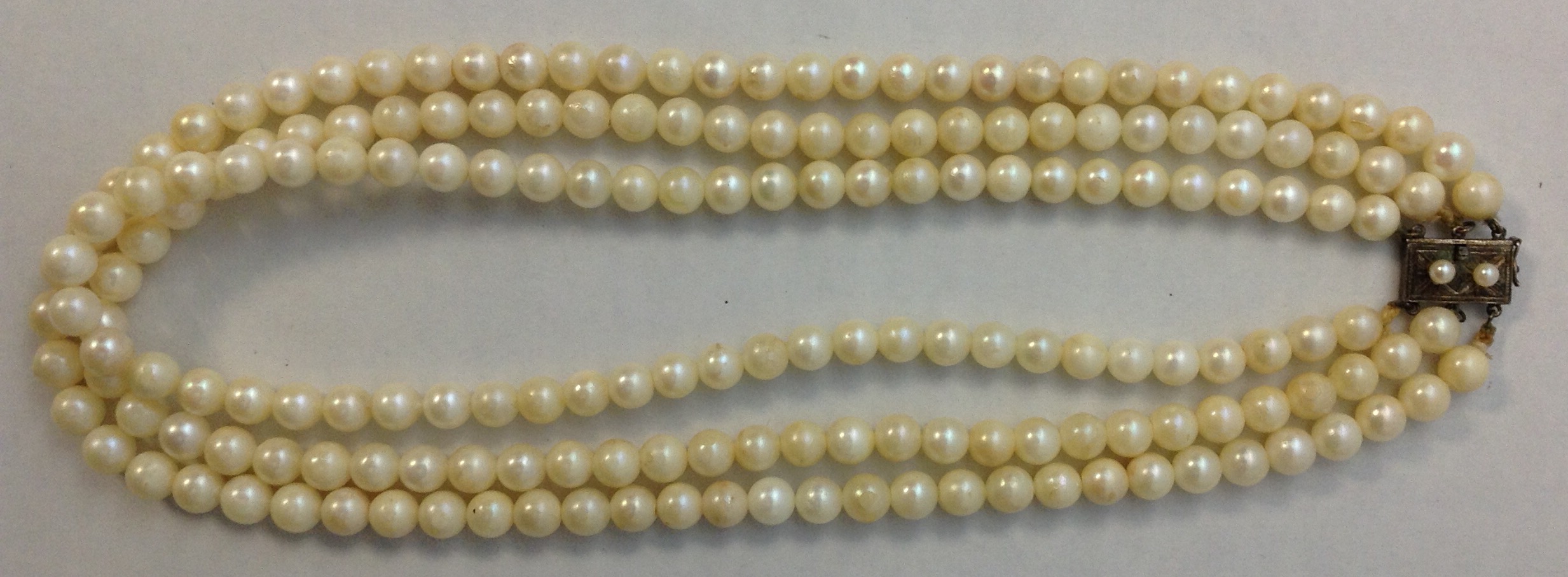 A VINTAGE THREE STRAND PEARL NECKLACE Having single rows of uniform pearls leading to a silver