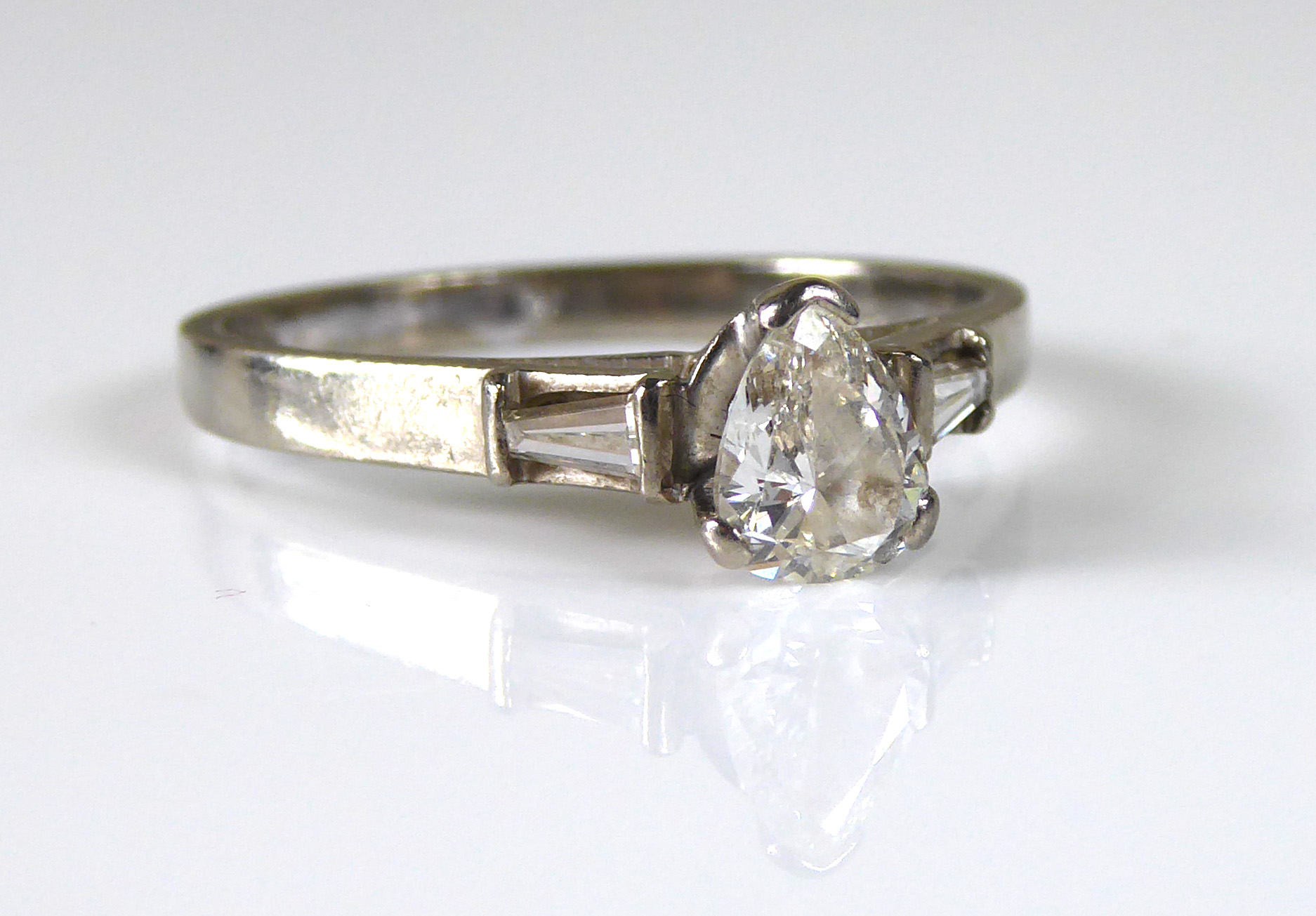 AN 18CT WHITE GOLD AND DIAMOND SOLITAIRE RING Having a pear cut diamond set between two tapering