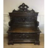 A VICTORIAN FINELY CARVED OAK HALL BENCH Having a hinged seat, the back decorated with a winged