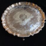 AN EARLY 20TH CENTURY SILVER SALVER Scalloped edge and scrolled feet, having an engraved floral