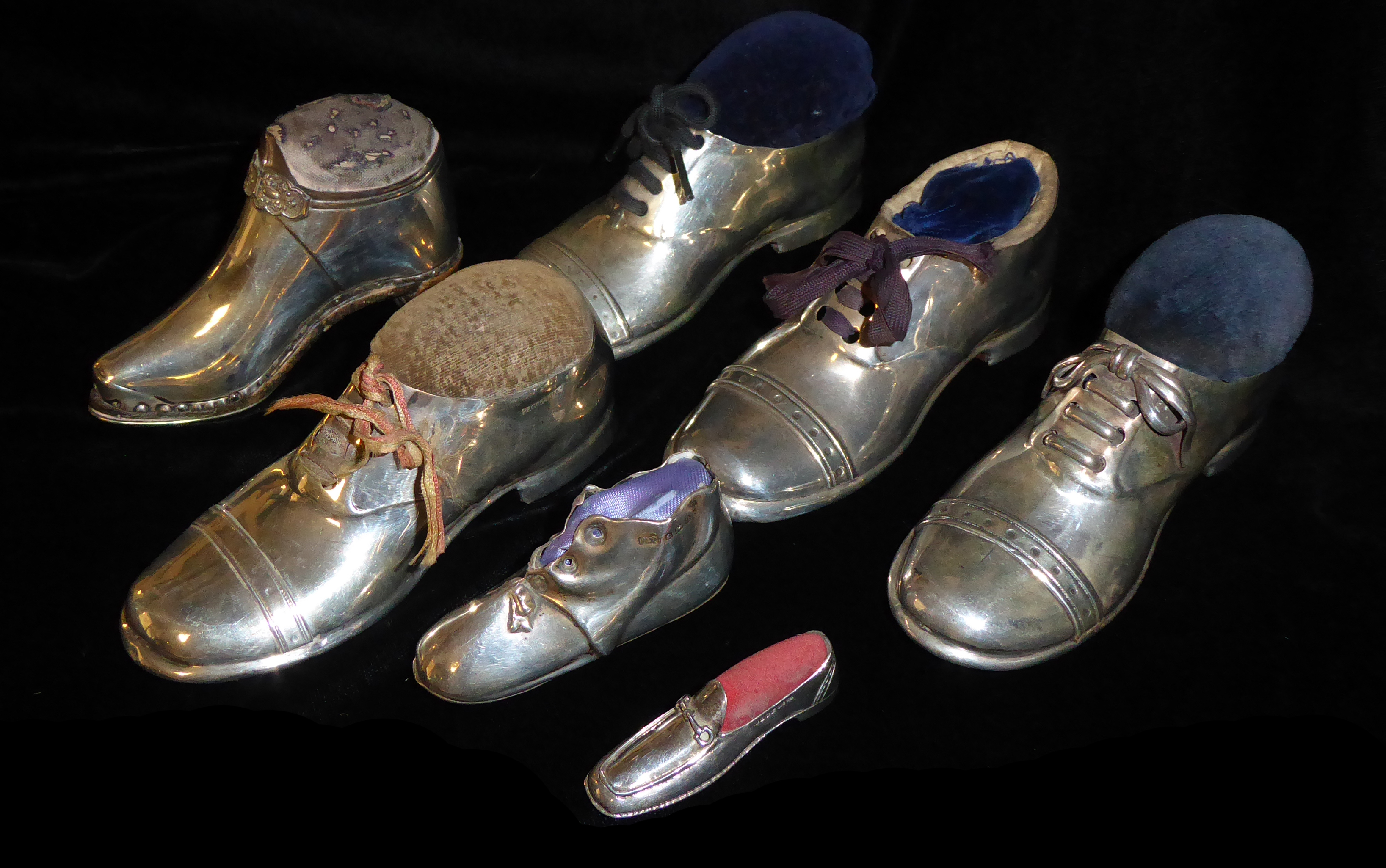 A COLLECTION OF FOUR EDWARDIAN NOVELTY SILVER SHOE PIN CUSHIONS Each having a wooden base, three