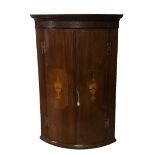 A GEORGIAN MAHOGANY BOW FRONTED CORNER CABINET The blind fret cornice above two doors finely