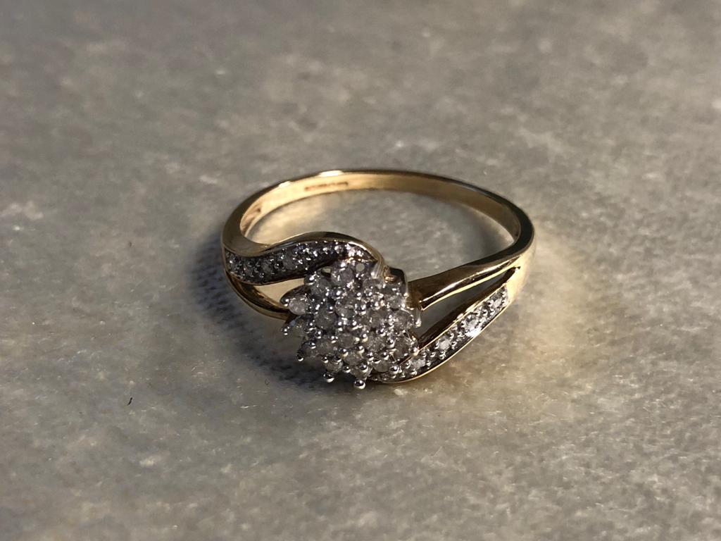 A 9CT GOLD AND DIAMOND CLUSTER RING HAVING A DAISY DESIGN IN THE MIDDLE WITH A DIAMOND CURVE