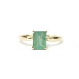 A 9ct gold single stone emerald cut emerald ring, to open shoulders and a plain polished shank, size