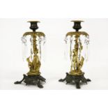 A pair of ormolu and bronze candle sticks, each with figural support and hanging cut glass lustre