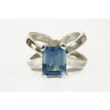 A silver single stone emerald cut blue topaz ring, with crossed head shoulders, 9.95g