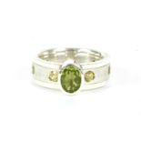 A silver single stone oval mixed cut peridot ring, rub set to a brush and polished band, set with