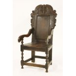 An oak wainscot armchair,with a carved and scrolled top rail, a plain panelled back, a solid