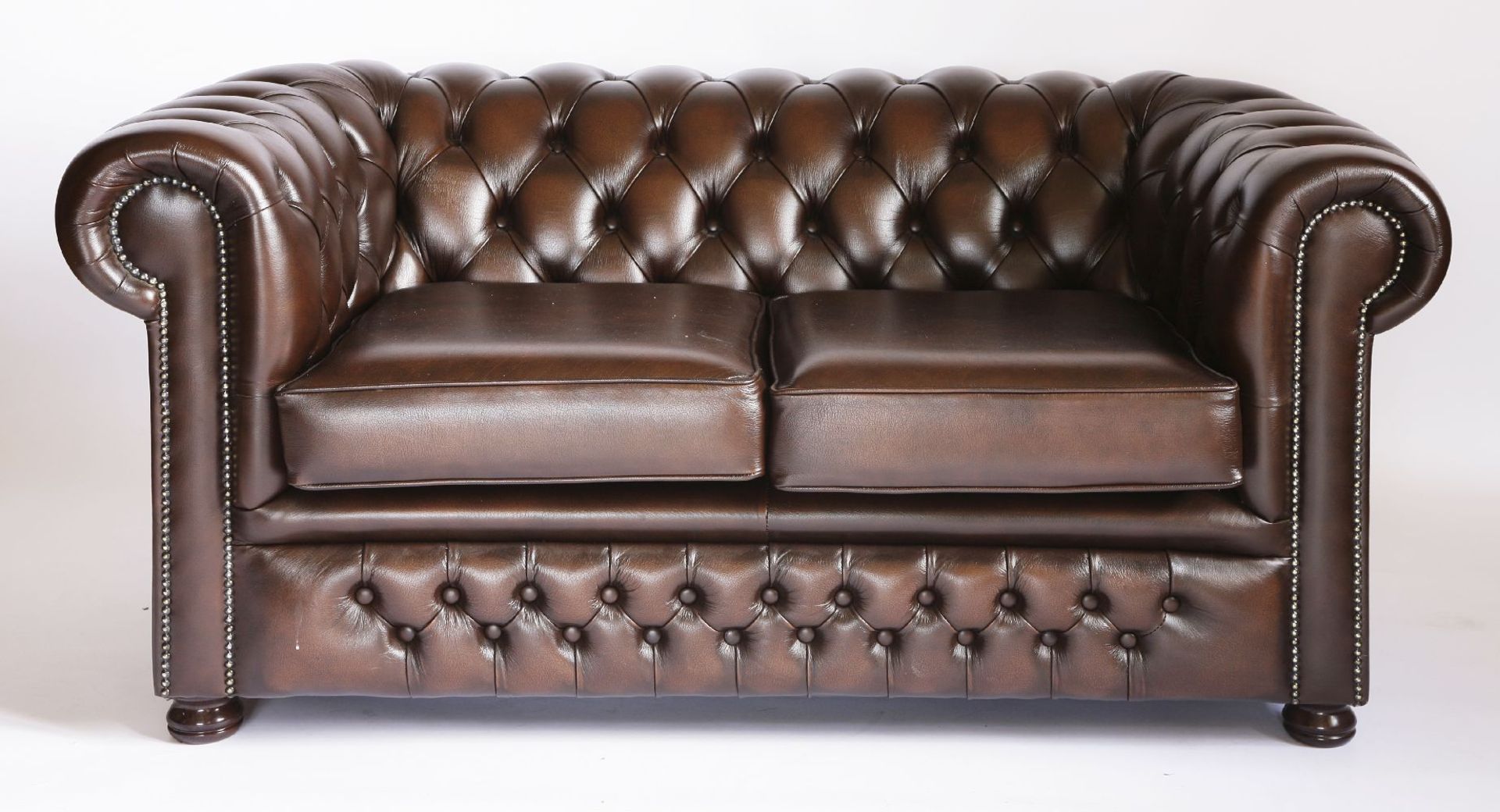 A modern brown leather two-seat chesterfield settee,with deep buttoned upholstery, seat cushions and