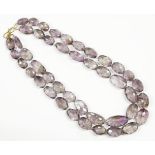 A two row graduated oval faceted amethyst bead necklace, strung knotted to a gilt metal hook clasp