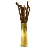 A collection of predominately carved root wood walking sticks, in a brass shell casing stand