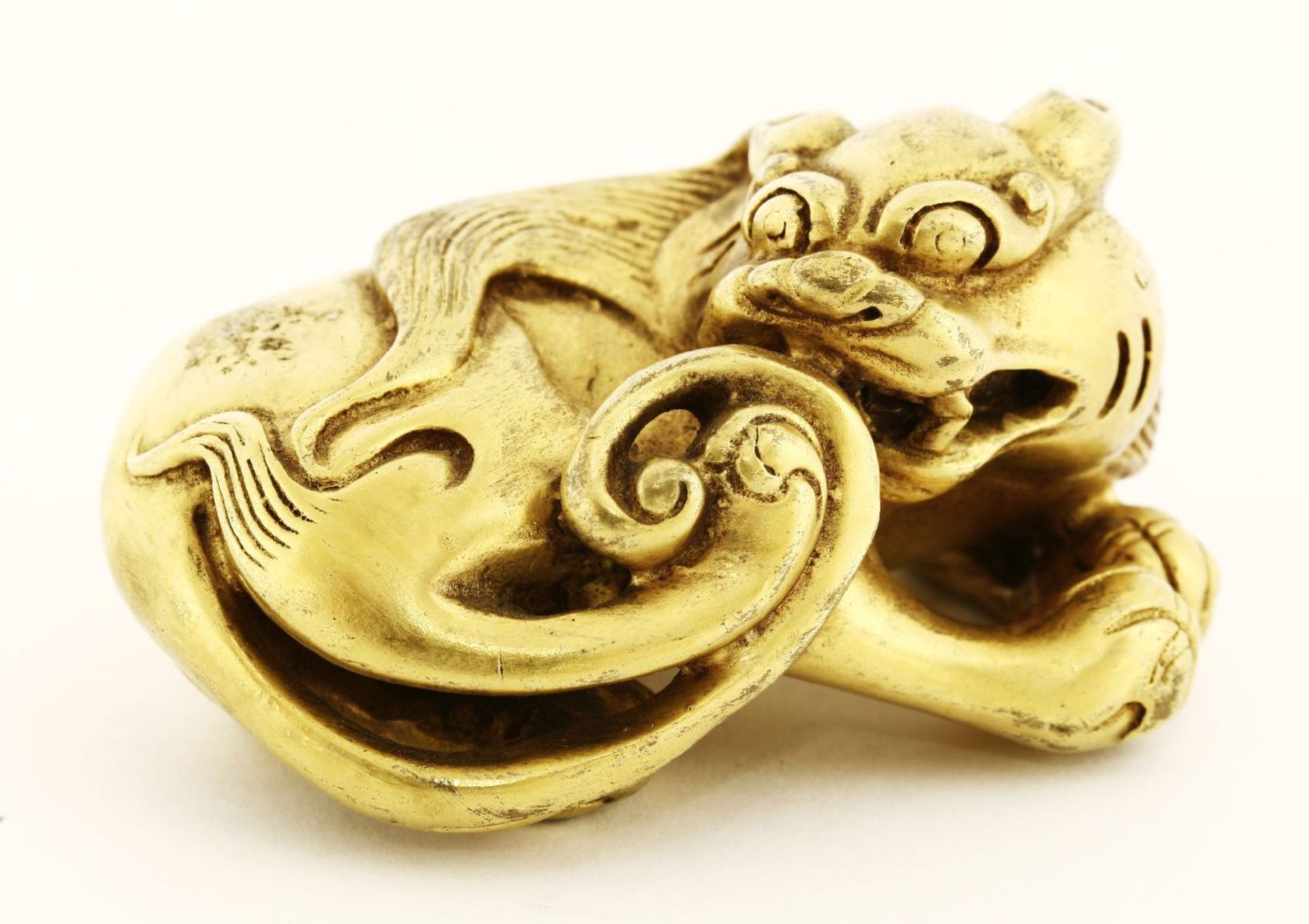A gilt bronze paper weight, of a recumbent mythical beast, its head tilted to reach its tail, 6.5cm