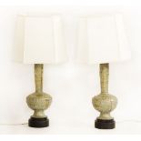 A pair of Indian cast gilt metal table lamps, with figural decoration, fitted cream shades, 85cm
