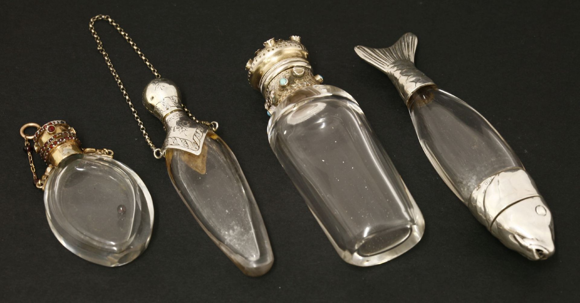 Four clear glass scent bottles,two with 'gem set' white metal covers,one of slender teardrop shape