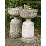 A pair of reconstituted garden urns,each with a shallow jardinière, raised on a socle and column,