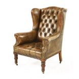 A leather wing-back armchair, with button back and seat, with turned supports