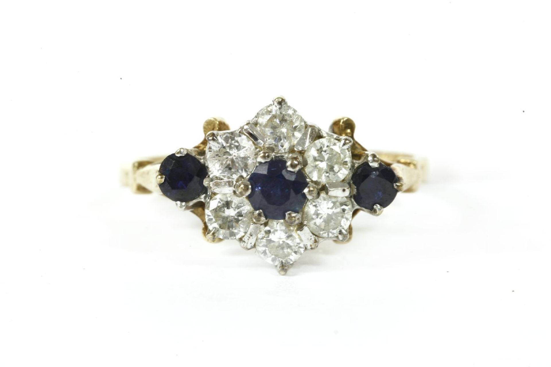 A 9ct gold sapphire and diamond cluster ring,with sapphire set shoulders, London 1981. 2.45g.