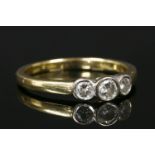 An 18ct gold three stone diamond ring, three brilliant cut diamonds rub set to white collets and a