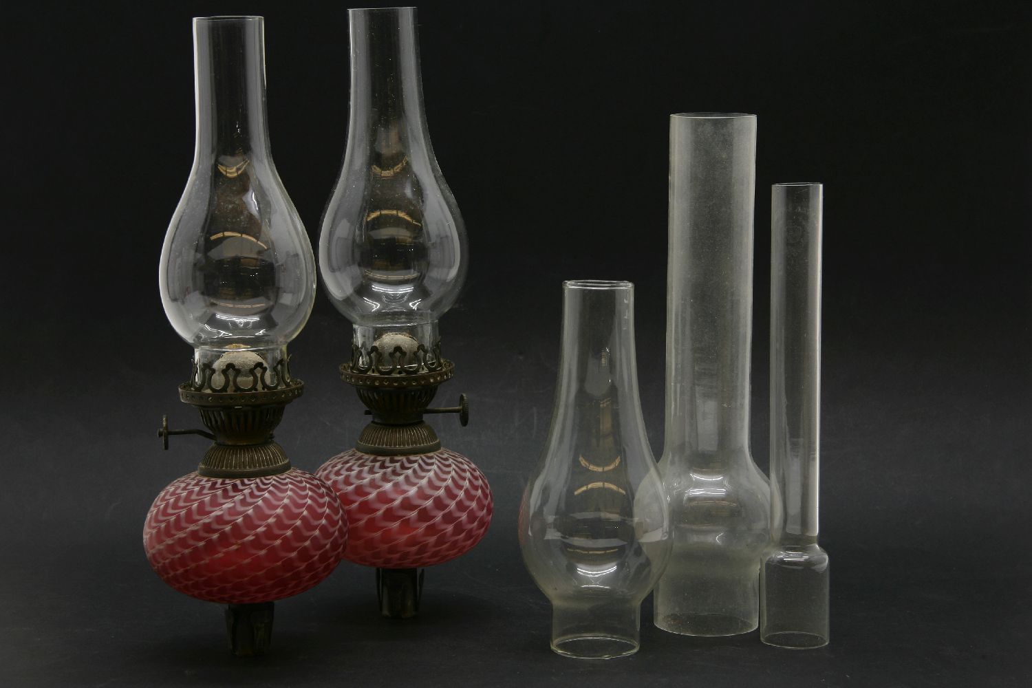 A pair of Victorian candlestick oil lamps, with red and white glass reservoirs and peg fittings,