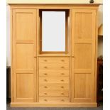 A bespoke pale oak wardrobe, by Henry Gordon-James, having a central bank of drawers, flanked by