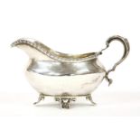 A silver sauce boat, with moulded scroll leaf handle and gadrooned border raised on four shell feet,