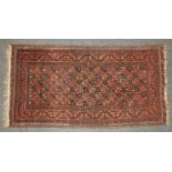 A hand knotted Bokhara rug, the brick red fields with repeating geometric decoration, with a