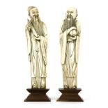 A pair of Chinese carved ivory figures of scholars, one holding a bamboo tube, the other a bag, on