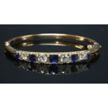 An Edwardian sapphire and diamond hinged bangle,with three oval graduated mixed cut sapphires,